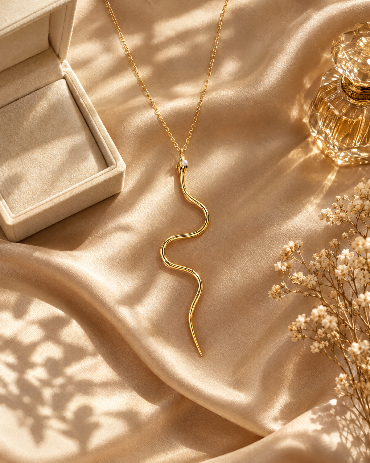 Gold serpent pendant necklace on champagne satin with a jewellery box and perfume bottle